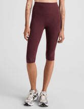 model is wearing red high-waisted pedal pusher length leggings.